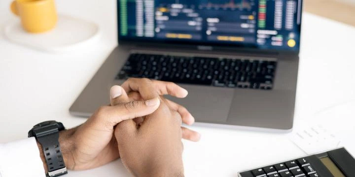 Homem fazendo análise de preços dos concorrentes em frente a um notebook com gráficos e uma calculadora ao lado direito.