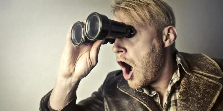 Homem surpreso observando com binóculo, simbolizando a análise detalhada dos backlinks dos concorrentes.